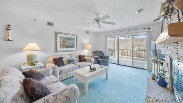 carpeted living area featuring a textured ceiling, a stone fireplace, visible vents, and a ceiling fan