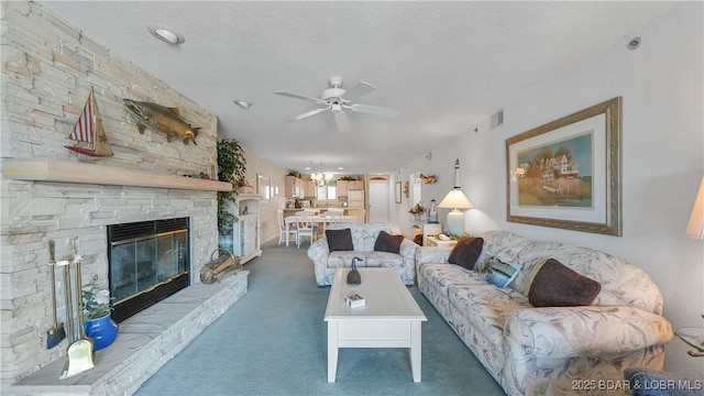 carpeted living room with a textured ceiling, a stone fireplace, ceiling fan with notable chandelier, and visible vents