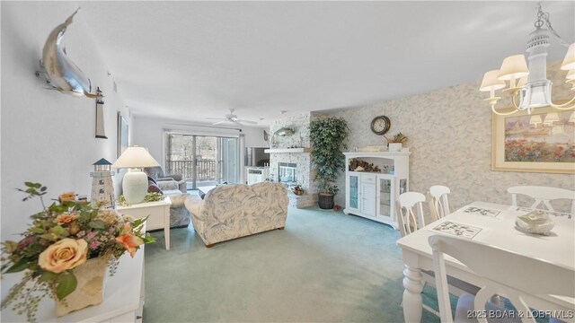 carpeted living area featuring ceiling fan with notable chandelier, a stone fireplace, and wallpapered walls