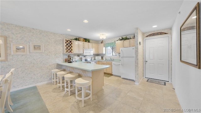 kitchen with white appliances, wallpapered walls, a peninsula, light countertops, and a kitchen bar