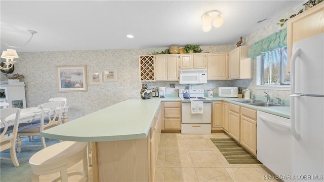 kitchen featuring light brown cabinets, a sink, white appliances, a peninsula, and wallpapered walls