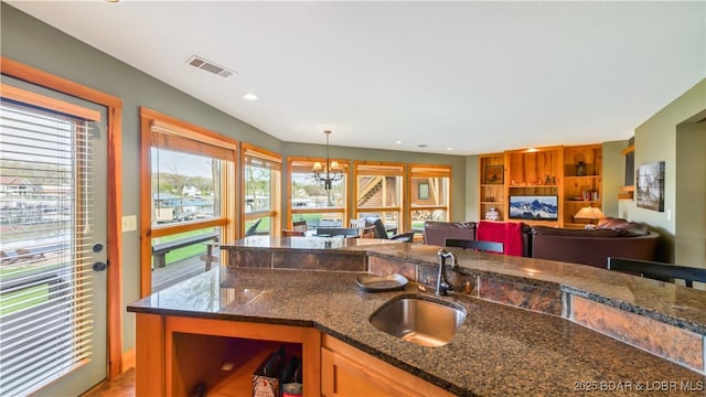 kitchen featuring visible vents, dark stone countertops, decorative light fixtures, a chandelier, and a sink