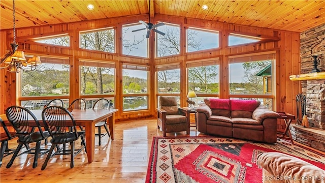 sunroom with lofted ceiling, wooden ceiling, a stone fireplace, and ceiling fan with notable chandelier