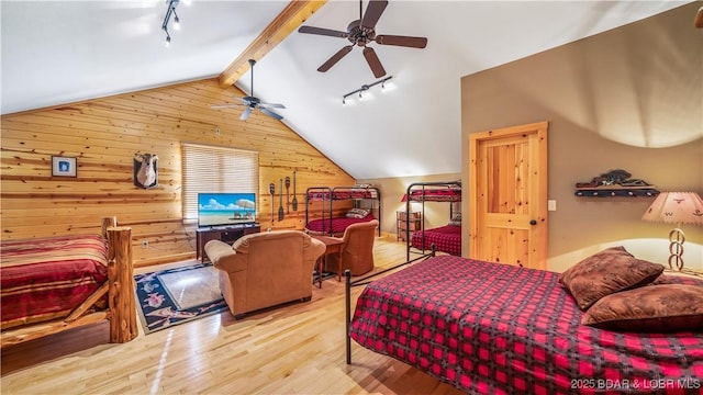 bedroom with vaulted ceiling with beams, rail lighting, wooden walls, and wood finished floors