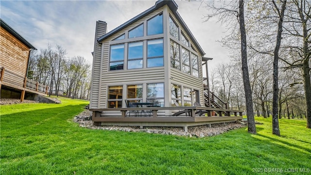 rear view of property featuring a chimney, a wooden deck, and a lawn