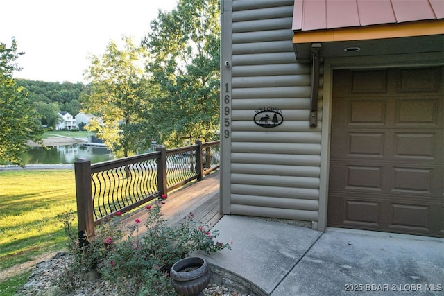 entrance to property with a garage, a deck with water view, log veneer siding, and a yard