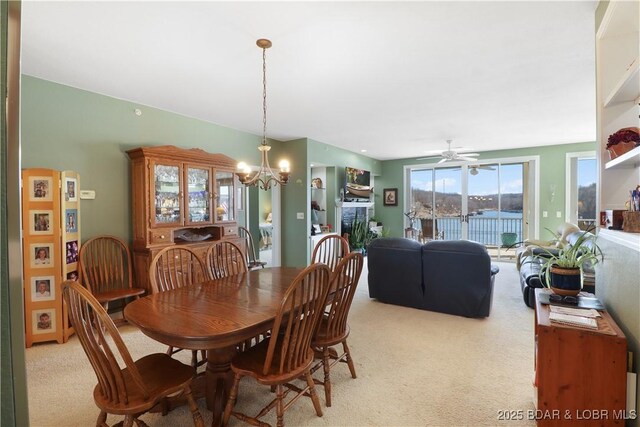 dining area with light carpet, a fireplace, and ceiling fan with notable chandelier