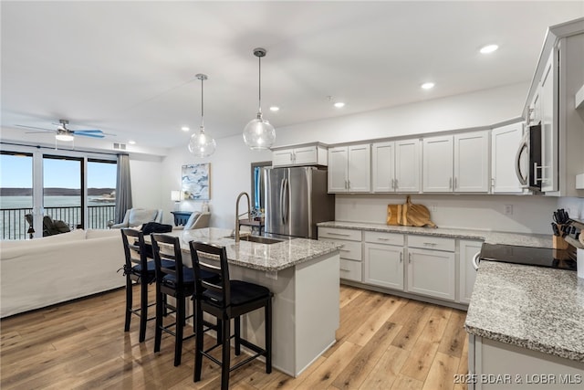 kitchen featuring open floor plan, stainless steel appliances, light wood-style floors, and a sink