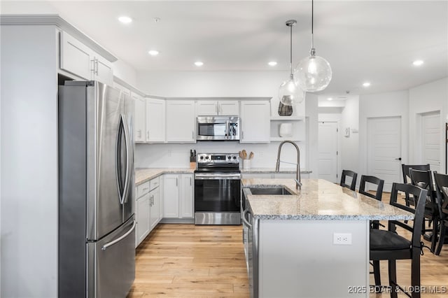 kitchen with open shelves, a sink, stainless steel appliances, light wood-style floors, and a kitchen breakfast bar