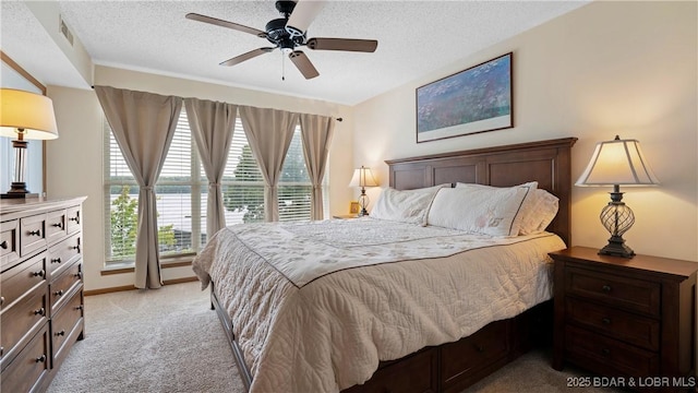 bedroom with baseboards, visible vents, light colored carpet, ceiling fan, and a textured ceiling