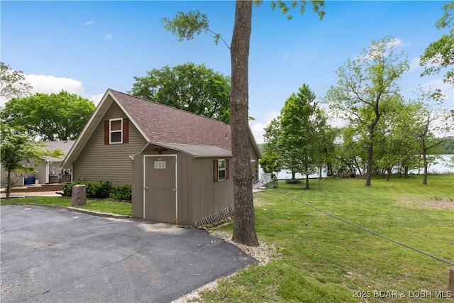 exterior space with a shed, roof with shingles, an outbuilding, and a yard