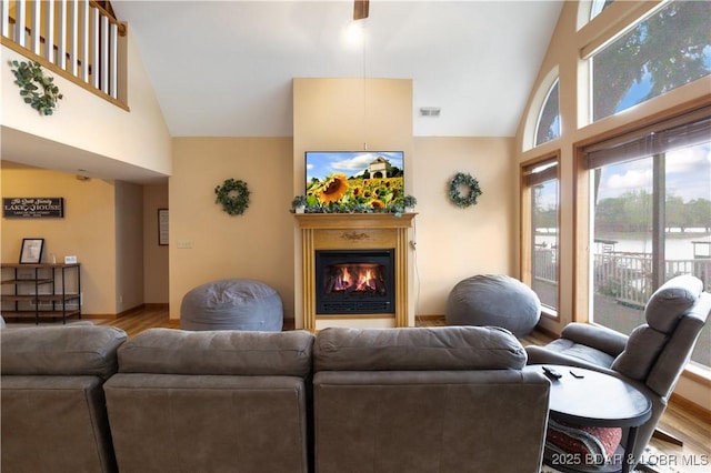 living room with high vaulted ceiling, a glass covered fireplace, and wood finished floors