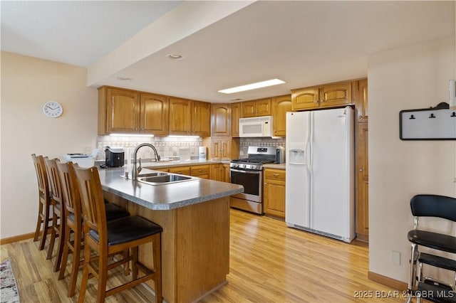 kitchen with a peninsula, white appliances, backsplash, and a sink