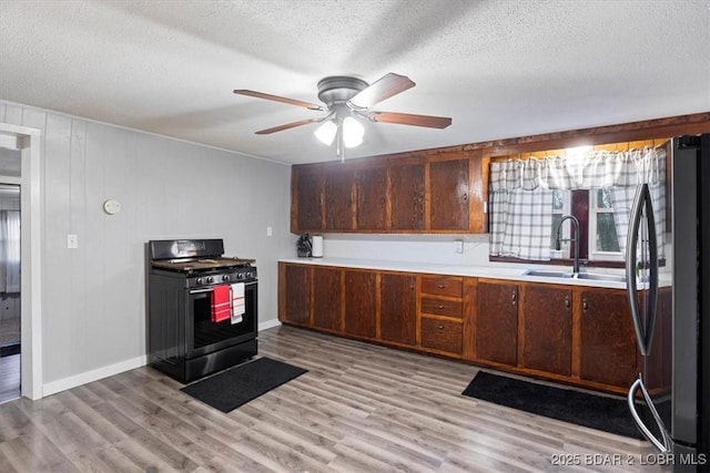 kitchen with light wood-type flooring, a sink, freestanding refrigerator, and range with gas stovetop