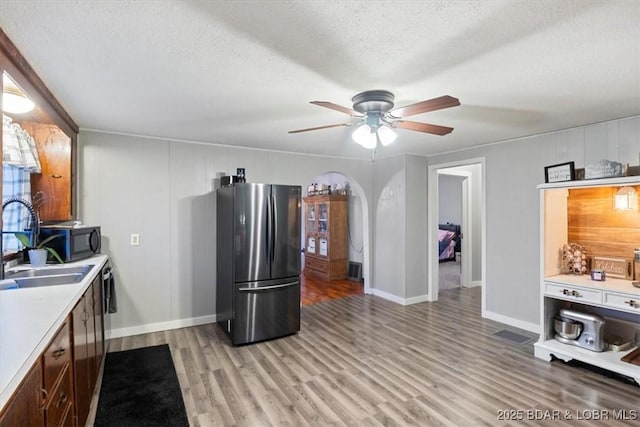 kitchen featuring light wood finished floors, freestanding refrigerator, light countertops, a textured ceiling, and a sink