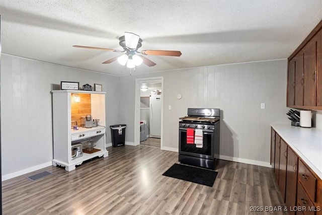 kitchen with stainless steel gas stove, wood finished floors, freestanding refrigerator, light countertops, and a textured ceiling