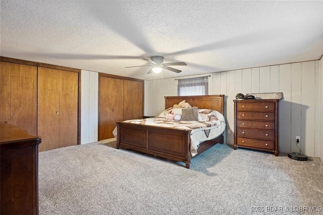 carpeted bedroom featuring multiple closets, ceiling fan, and a textured ceiling