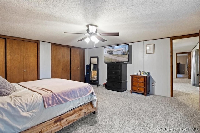 carpeted bedroom with a ceiling fan, a textured ceiling, and two closets