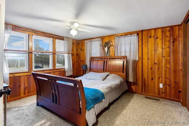 bedroom with light carpet, ceiling fan, wood walls, and visible vents