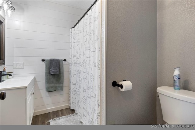 bathroom with a textured wall, toilet, a shower with shower curtain, wood finished floors, and vanity