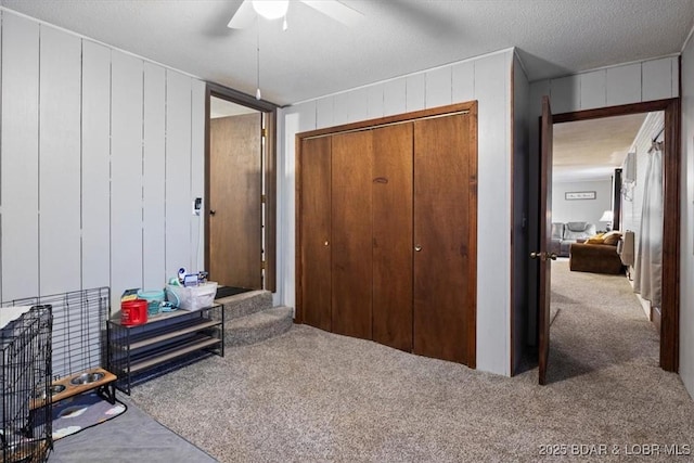 carpeted bedroom with a ceiling fan, a closet, wood walls, and a textured ceiling