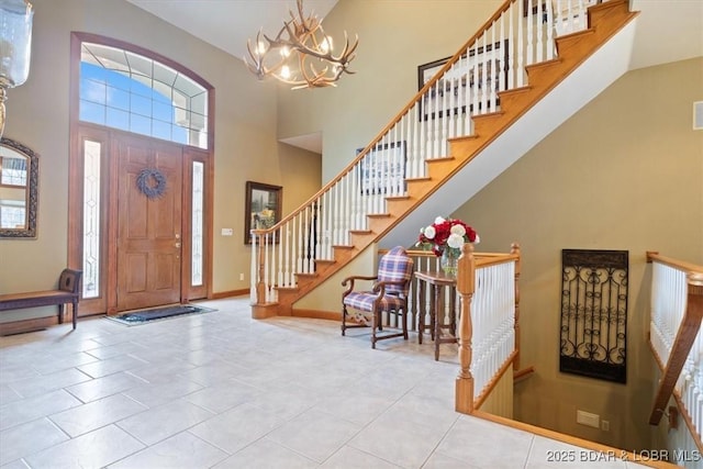 tiled entryway featuring a chandelier, a high ceiling, a wealth of natural light, and baseboards