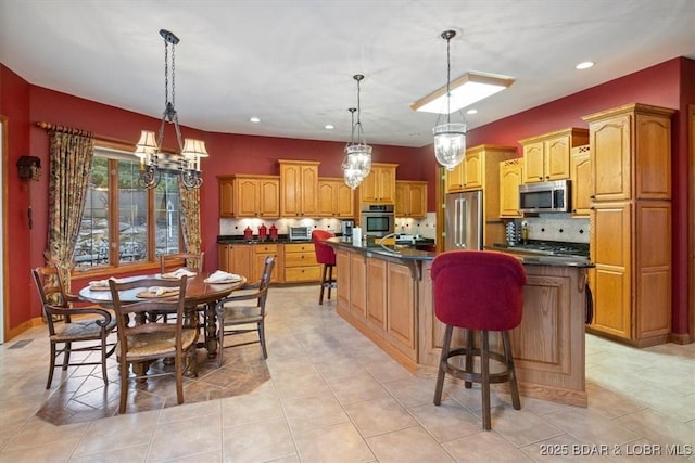 kitchen with a center island with sink, decorative backsplash, dark countertops, appliances with stainless steel finishes, and a kitchen breakfast bar