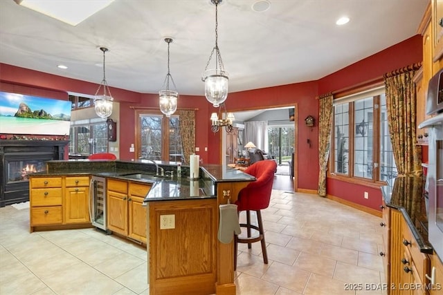 kitchen with a glass covered fireplace, a sink, an island with sink, beverage cooler, and a kitchen breakfast bar