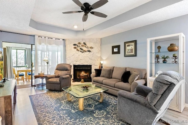 71 Costa Del Sol Dr Unit 207, Lake Ozark, MO 65049 - living room featuring a stone fireplace, a textured ceiling, a ceiling fan, and a raised ceiling