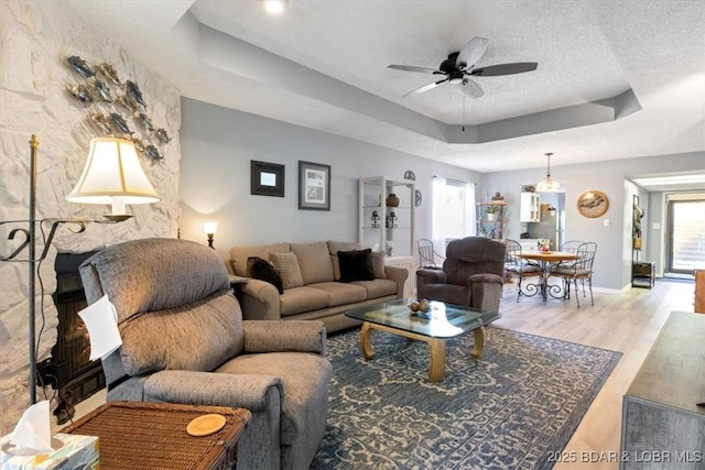 living area with a raised ceiling, ceiling fan, a textured ceiling, wood finished floors, and baseboards