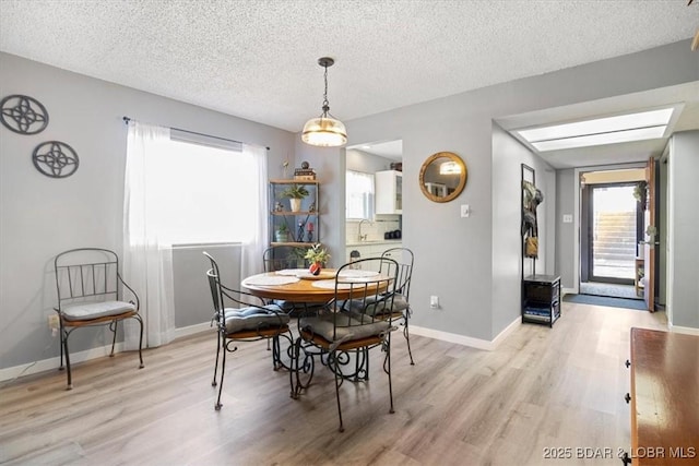 dining space with baseboards, a textured ceiling, and light wood finished floors