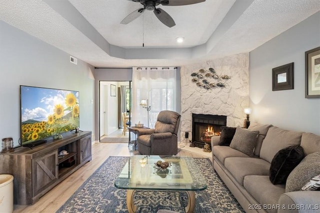 71 Costa Del Sol Dr Unit 207, Lake Ozark, MO 65049 - living area with light wood-style floors, a fireplace, a tray ceiling, a ceiling fan, and visible vents