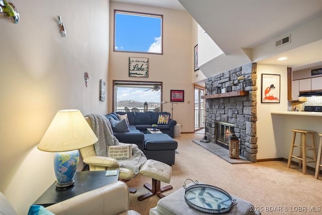 carpeted living room featuring visible vents, a fireplace, a high ceiling, and baseboards