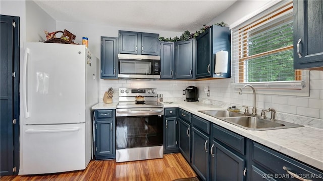 kitchen with appliances with stainless steel finishes, light countertops, a sink, and light wood finished floors