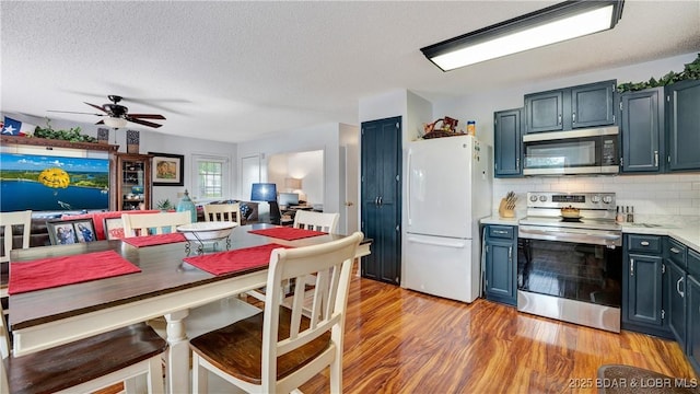 kitchen featuring light wood finished floors, appliances with stainless steel finishes, blue cabinets, light countertops, and backsplash