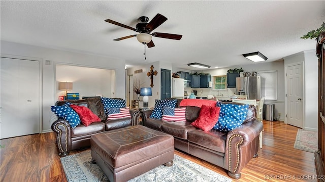 living area with a textured ceiling, ceiling fan, visible vents, and light wood-style floors