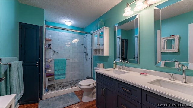 full bathroom with a shower stall, a textured ceiling, a sink, and wood finished floors