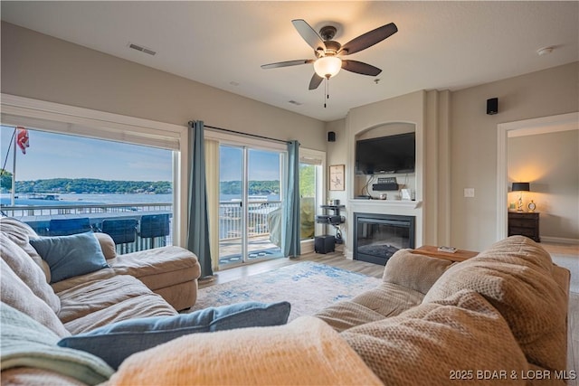 living room featuring visible vents, wood finished floors, a ceiling fan, and a glass covered fireplace