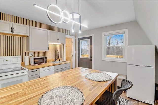 kitchen featuring pendant lighting, a breakfast bar area, butcher block counters, a sink, and white appliances