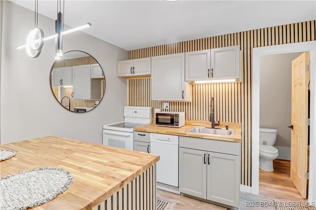 kitchen featuring decorative light fixtures, light wood finished floors, butcher block counters, a sink, and white appliances