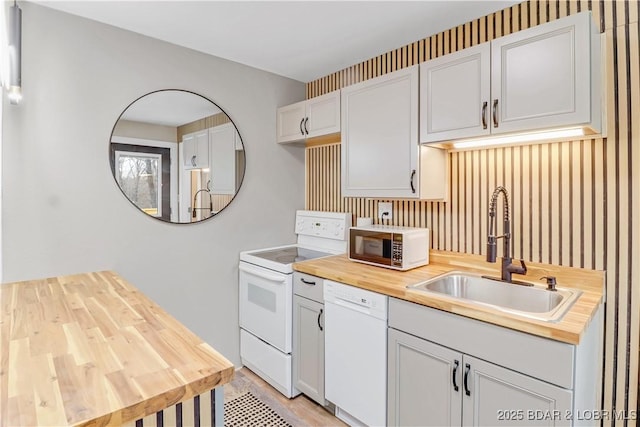 kitchen with a sink, white appliances, butcher block counters, and white cabinetry