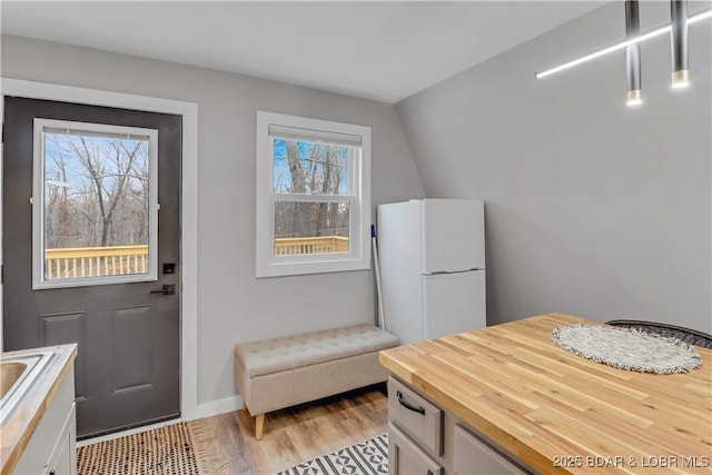 kitchen featuring light wood-style flooring, freestanding refrigerator, white cabinetry, and wood counters