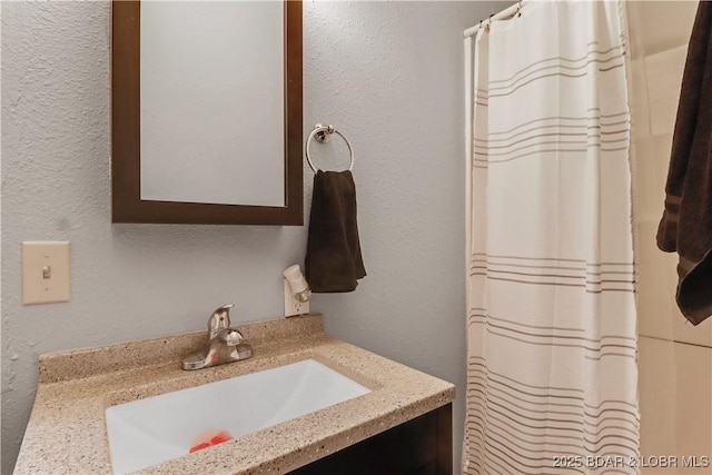 full bathroom featuring a shower with curtain, a textured wall, and vanity