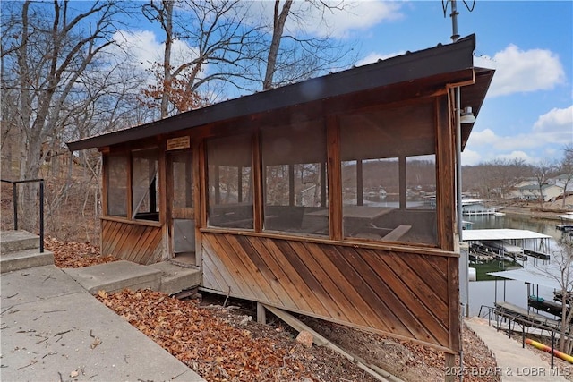 exterior space featuring a dock, a sunroom, and a water view