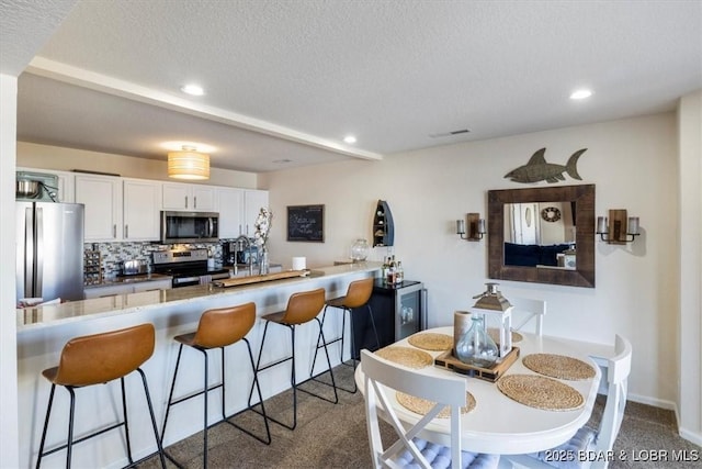 488 Regatta Bay Dr Unit 2C, Lake Ozark, MO 65049 - kitchen featuring appliances with stainless steel finishes, a textured ceiling, a breakfast bar area, white cabinets, and tasteful backsplash