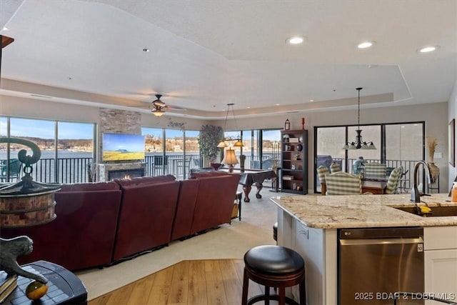 kitchen with a raised ceiling, stainless steel dishwasher, open floor plan, a sink, and light stone countertops