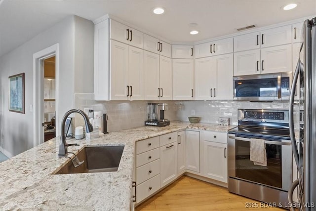 kitchen with backsplash, light wood-style flooring, appliances with stainless steel finishes, white cabinets, and a sink