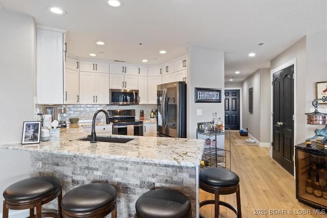 kitchen featuring stainless steel appliances, a peninsula, a sink, white cabinets, and light wood-type flooring