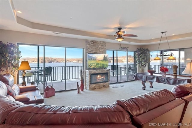 living area featuring plenty of natural light, carpet, a tray ceiling, and a stone fireplace