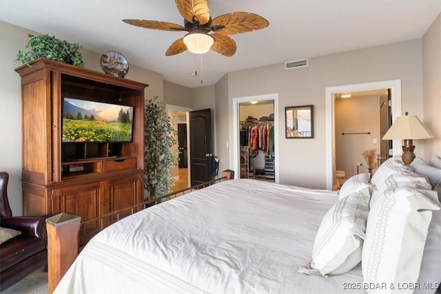 bedroom with a walk in closet, a closet, visible vents, a ceiling fan, and ensuite bath